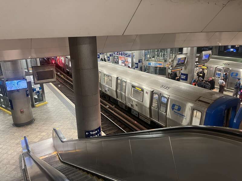 The platforms at the Journal Square PATH station, as viewed from an upper level. A Hoboken/33rd Street train prepares for its return trip, while a WTC train comes in from Newark.