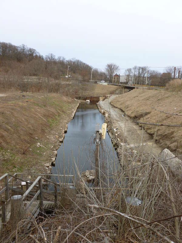 Looking west over small tailrace about 1000 feet east of Stone Mill, near 1 Canal Street, Lawrence, Massachusetts.  In the background is the junction between this former tailrace channel and the Spicket River. This tailrace has been covered over