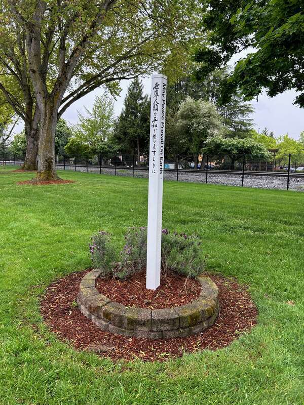 Pole that reads "may peace prevail on earth" in several languages at the Burlington Green-Yangzhou Park in Kent, Washington.