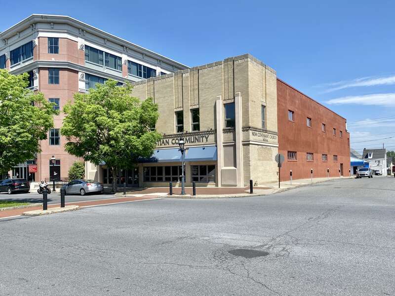 Built in the early 20th Century, this Art Deco-style building features a buff brick front facade and stucco-clad sides, stone trim, recessed panels above the window openings, decorative trim above the windows and below the parapet cap, decorative