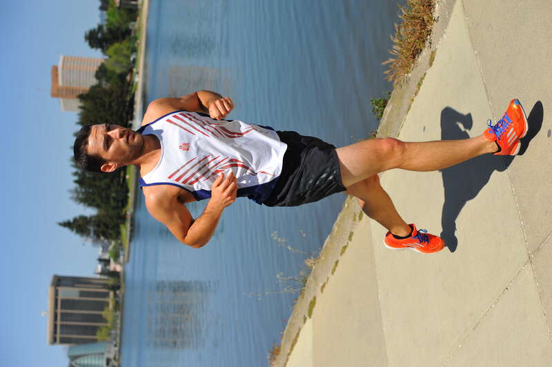Wearing a singlet (tank top) with the coveted M-dot logo this athlete jogs along Lake Merritt in Oakland.  His bright orange Adidas running shoes with blue shoe laces bring color to the lower part of the image.  View at a larger size to see the