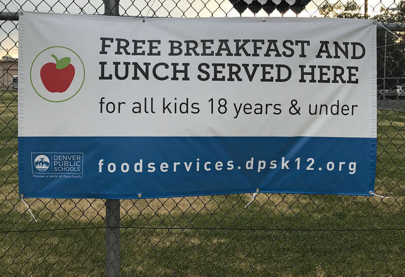 A sign that reads "Free Breakfast and Lunch Served Here for all kids 18 years and younger" hanging on a fence at West High School in Denver.