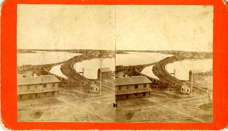 Aerial view looking toward the North River at the Eastern Railroad tracks, which appears to have been taken from the back of one of the courthouses on Federal Street. Train cars are visible along with the "Lowell &amp; Northern R.R. Depot" building,