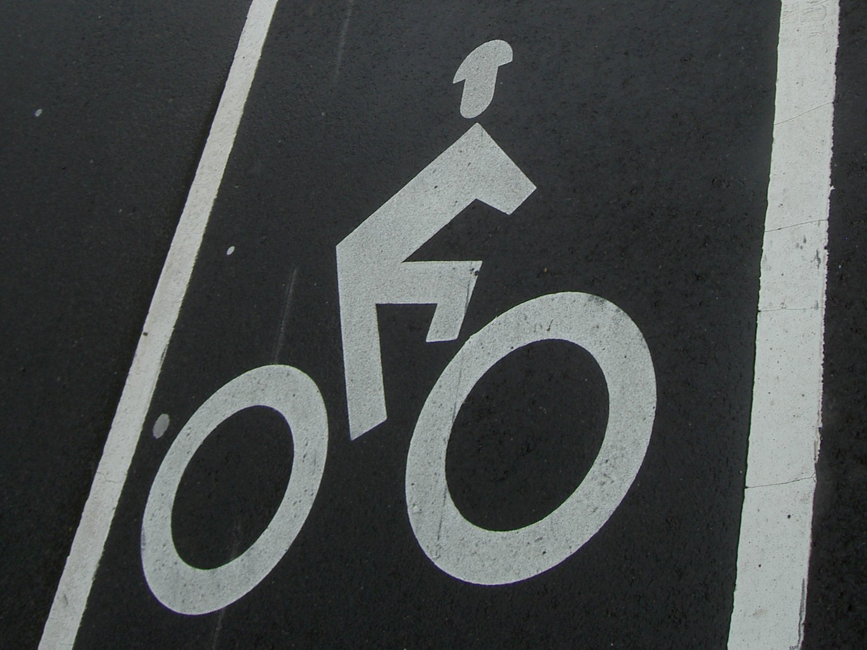 the bike lane is indicated with this painting on the asphalt.  It amuses me that the little bicyclist is wearing a helmet.
