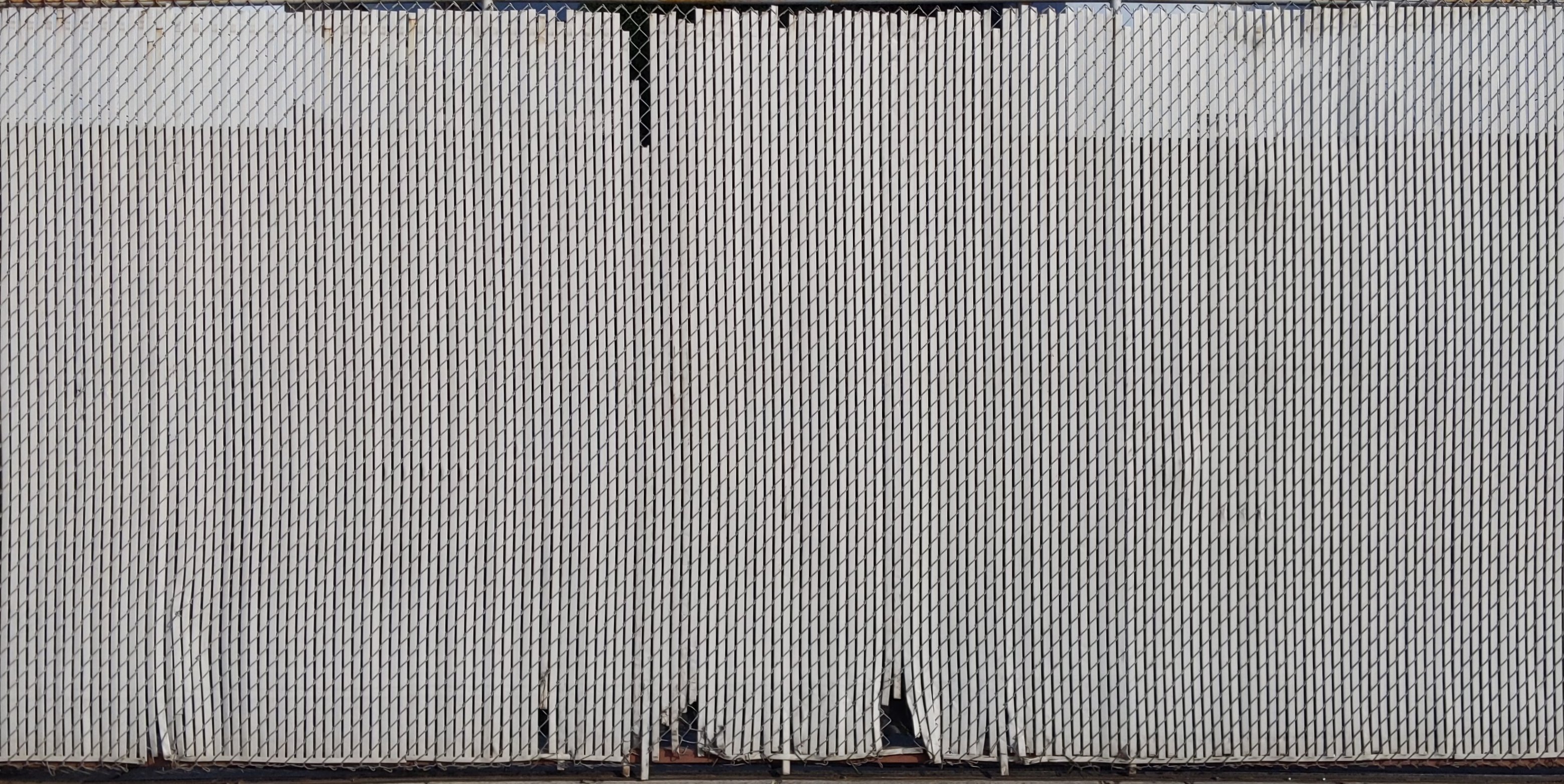 A chain link fence with vertical plastic slats. Image will tile seamlessly horizontally.