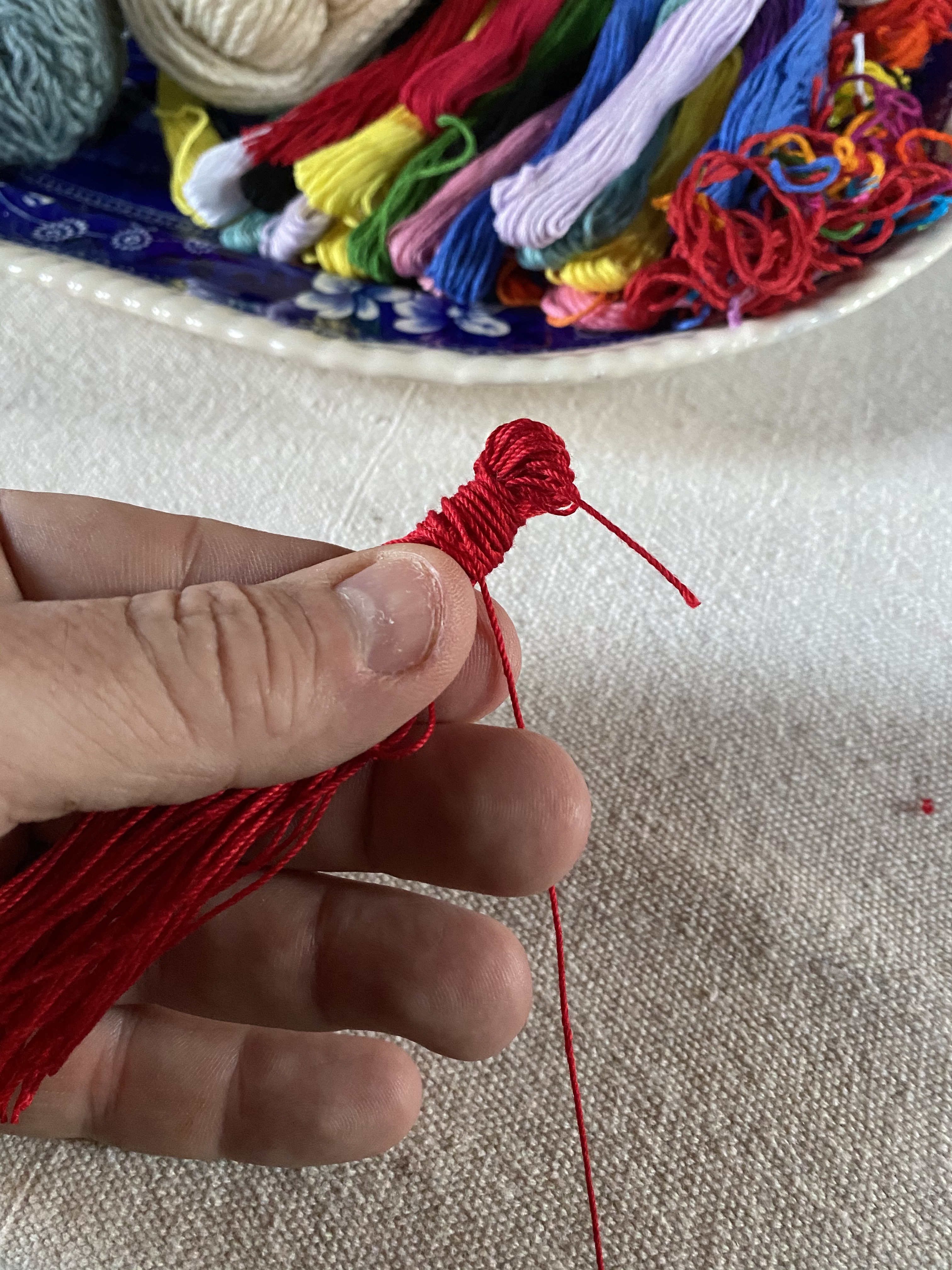 A bunch of red embroidery floss, folded in half, and wrapped with more red embroidery floss.
Cut a 10-inch piece of string. You can match the color to your tassel or use a contrasting color. Tie the string around the tassel, ½ inch down from the top.