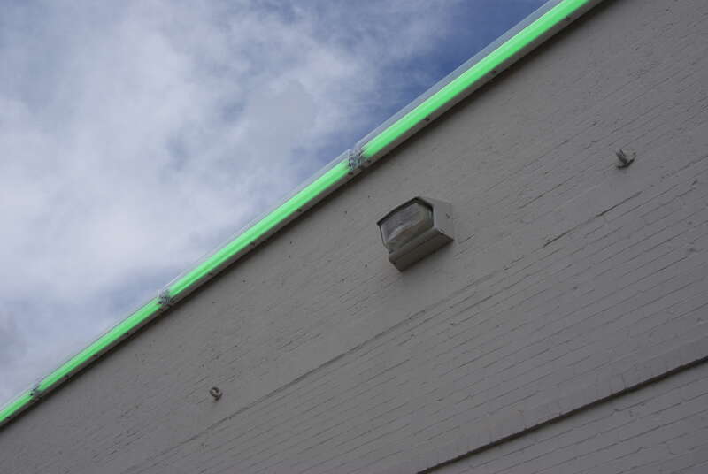 The work consists of two rows of green fluorescent light tubes, one installed on the east and the other on the west top edge of Richmond Hall of The Menil Collection at 1500 Richmond Avenue, Houston, Texas, USA. This photograph shows the tubes on the