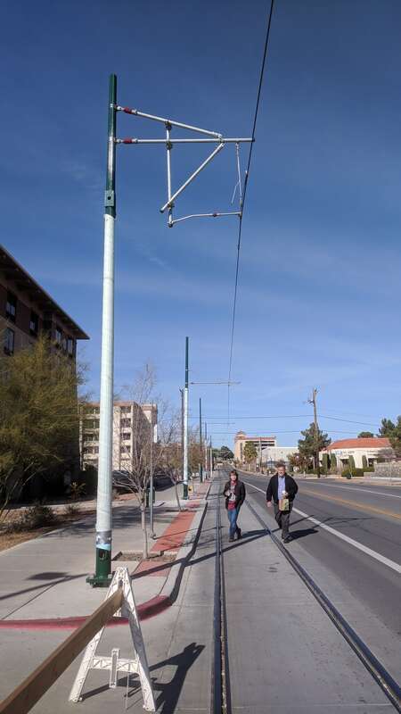 Overhead electric infrastructure and rails for the under-construction El Paso Streetcar system at the Univerity/Oregon stop, with pedestrians.