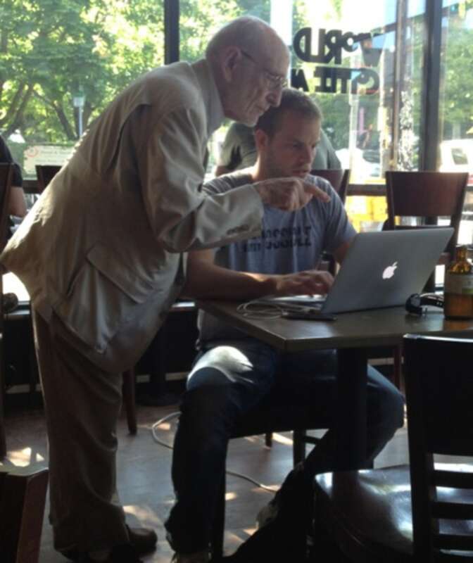Russell Kirsch standing over and pointing to a laptop computer being used by Joel Runyon seated at a table.