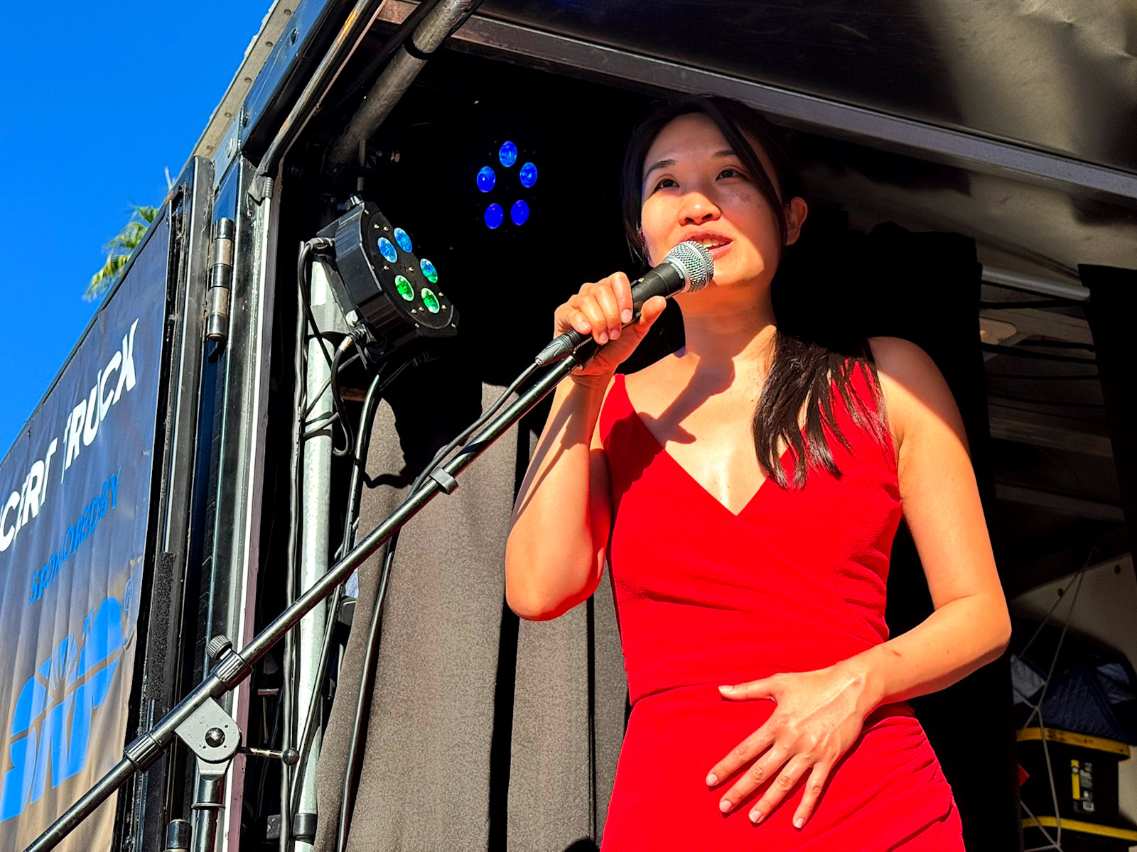 Susan Zhang speaking at outdoor concert presented by The Concert Truck at Chandler Farmers Market, Dr. A. J. Chandler Park, Oct 25, 2025. Chandler, Arizona. Sponsored by Chandler Center for the Arts and KBACH Radio. Performed by Kevin Ahfat and Susan